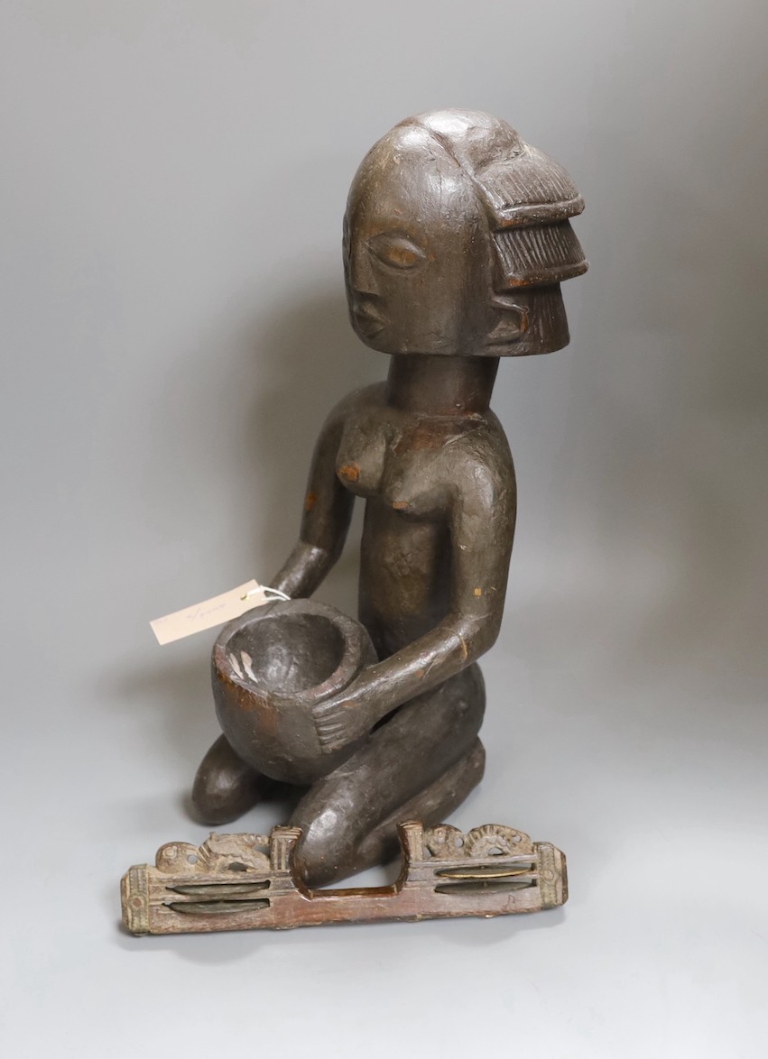 An African tribal carved wood kneeling figure holding bowl (44cm high) and tribal hand instrument (2)